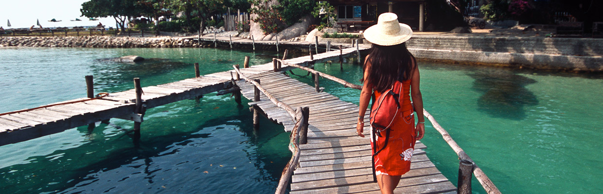 Woman walking on wooden bridge over lake; image used for HSBC Singapore travel and leisure rewards.